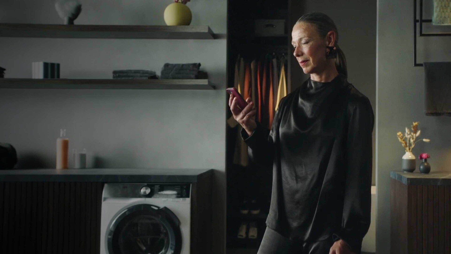 Vrouw in een kamer met een AEG wasmachine en een smartphone waarmee zij de wasmachine kan bedienen.